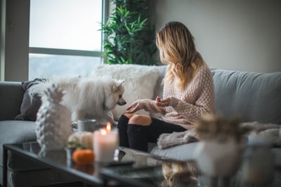 woman and white dog sitting on a couch - white candle lit on coffee table with white pineapple thinking about refinancing